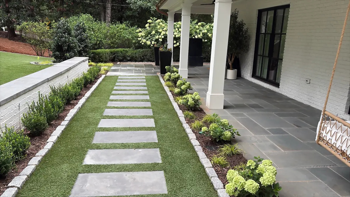 Bluestone stepping stones set into a turf strip, running past hydrangeas to a covered bluestone porch